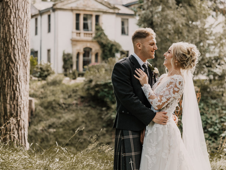 Smiling bride and groom embrace outside Norwood Hall Hotel in Aberdeen